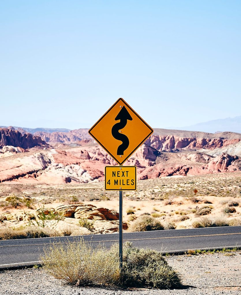 traffic sign showing curved road next 4 miles