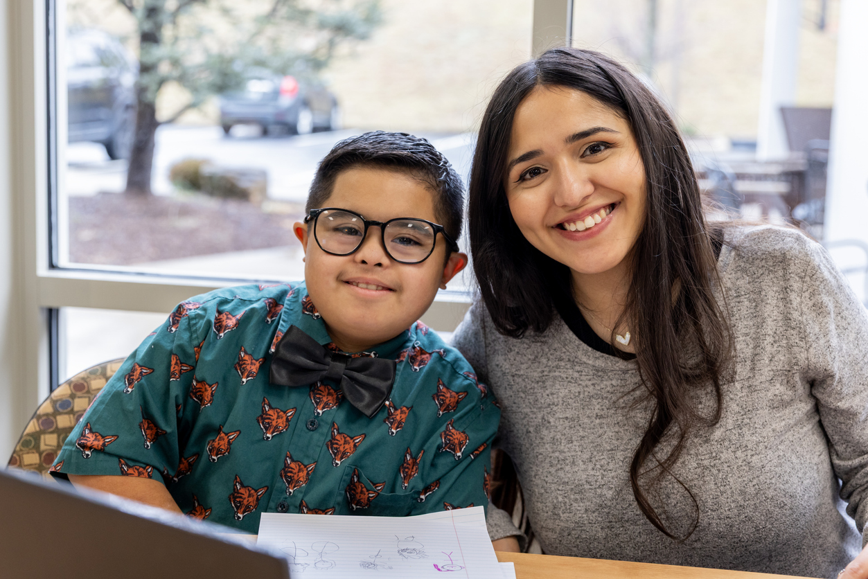 A Hispanic woman offers one-on-one academic assistance to a teenage boy in a classroom setting, highlighting engaged and supportive learning.